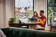 Man and woman sitting next to each other at a table in a cafe with a standing tablet.