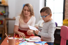 Female teaching assistant helping a SEN child with a crafts project, sat at a table using pens and paper.