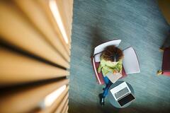 Aerial view of woman writing in a notebook with a laptop infront to her.