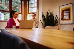 Female sitting at a table looking at her laptop with smiling male next to her at home
