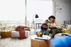 male sitting on couch holding a notebook and pen. Showing his notebook to a kid.
