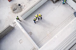Arial view of construction workers on a roof top with clipboards, talking.