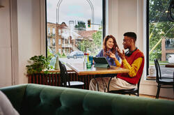 Man and woman sitting next to each other at a table in a cafe with a standing tablet.