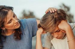 woman sat next to a young boy, with her hand on his head in support