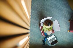 Aerial view of woman writing in a notebook with a laptop infront to her.