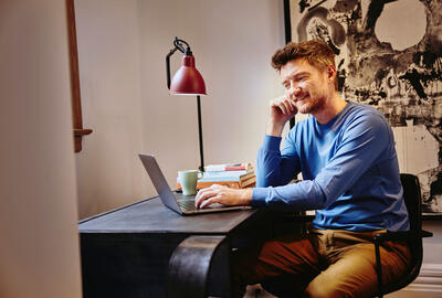 Male in a blue shirt sitting at a desk working on his laptop