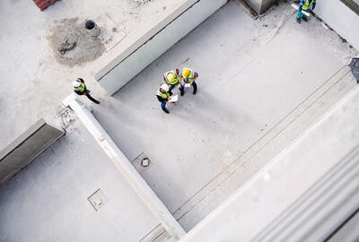 Arial view of construction workers on a roof top with clipboards, talking.
