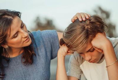 woman sat next to a young boy, with her hand on his head in support