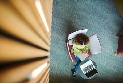 Aerial view of woman writing in a notebook with a laptop infront to her.