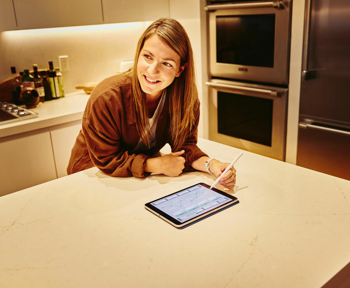 Female, smiling, working on tablet in kitchen on kitchen counter looking away from tablet