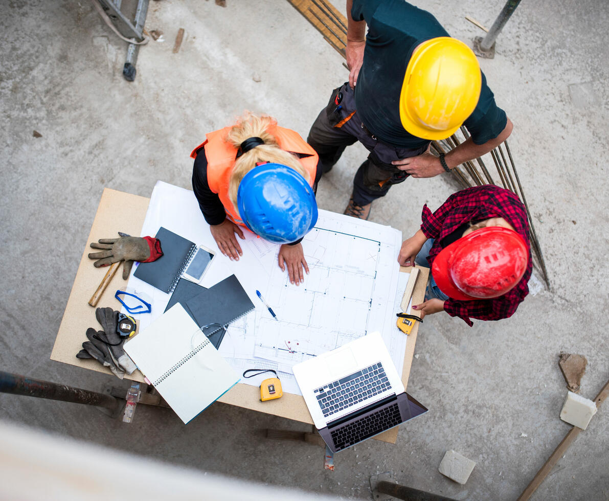 Three workers examining blueprints on a construction site