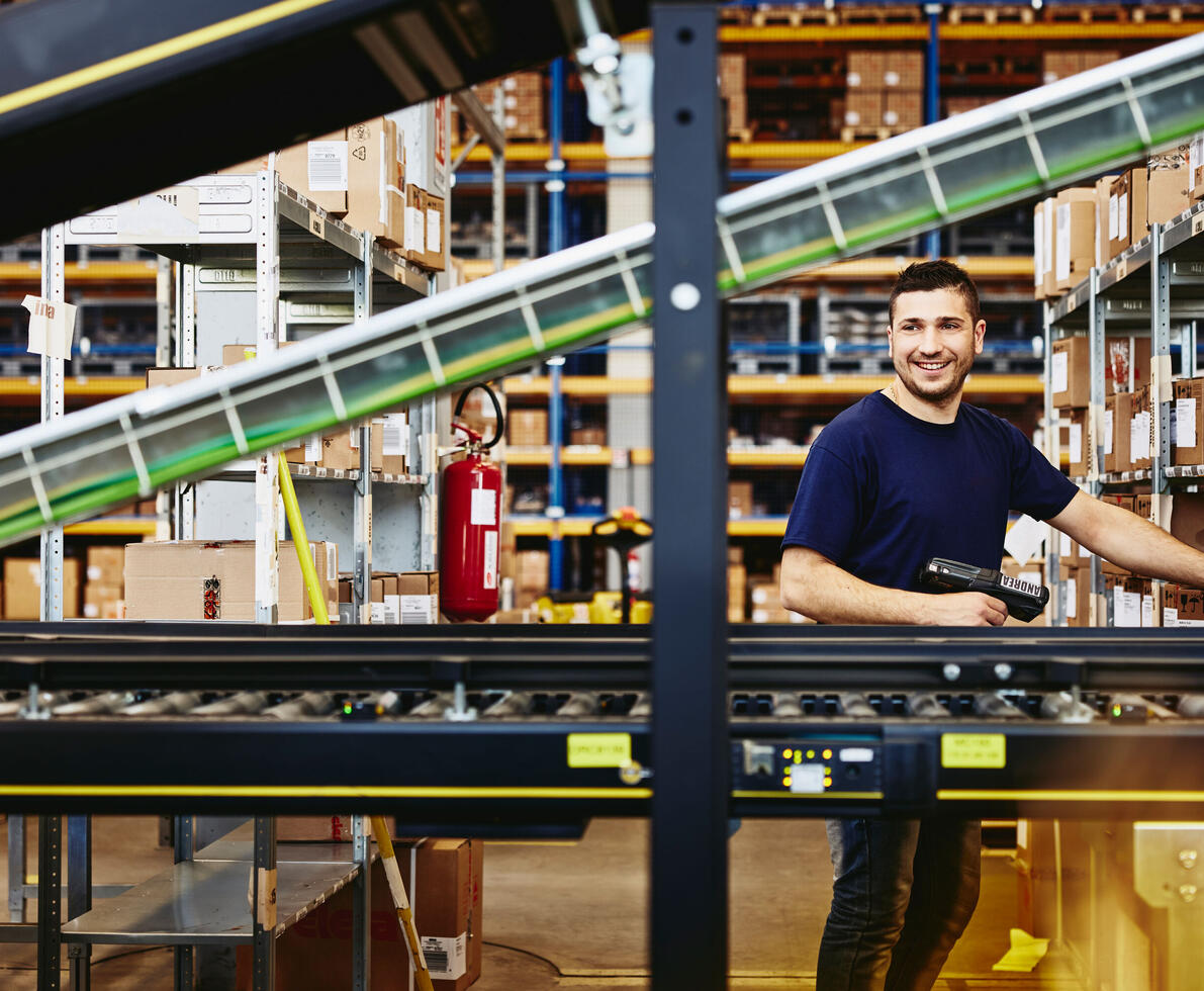 Smiling male standing behind a conveyor belt.