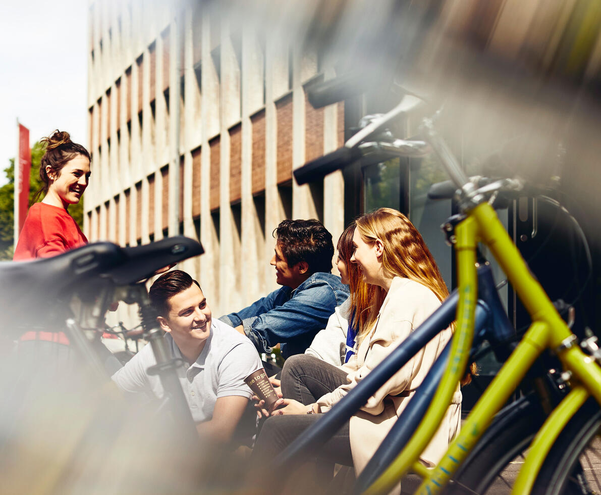A group of students sitting outside a building on some steps next to bikes.