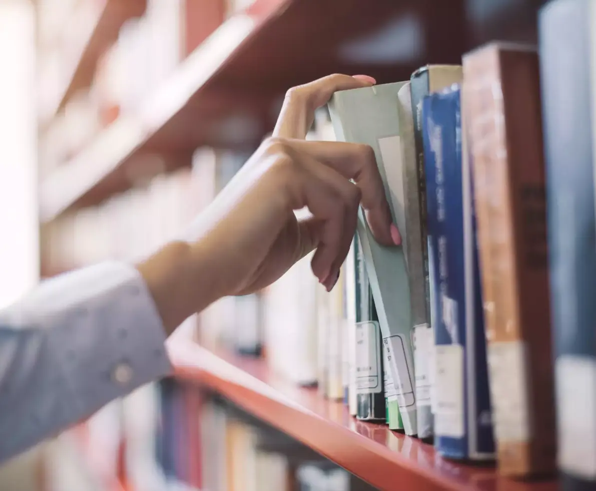 Woman at the library, she is searching books on the bookshelf and picking a textbook, hand close up