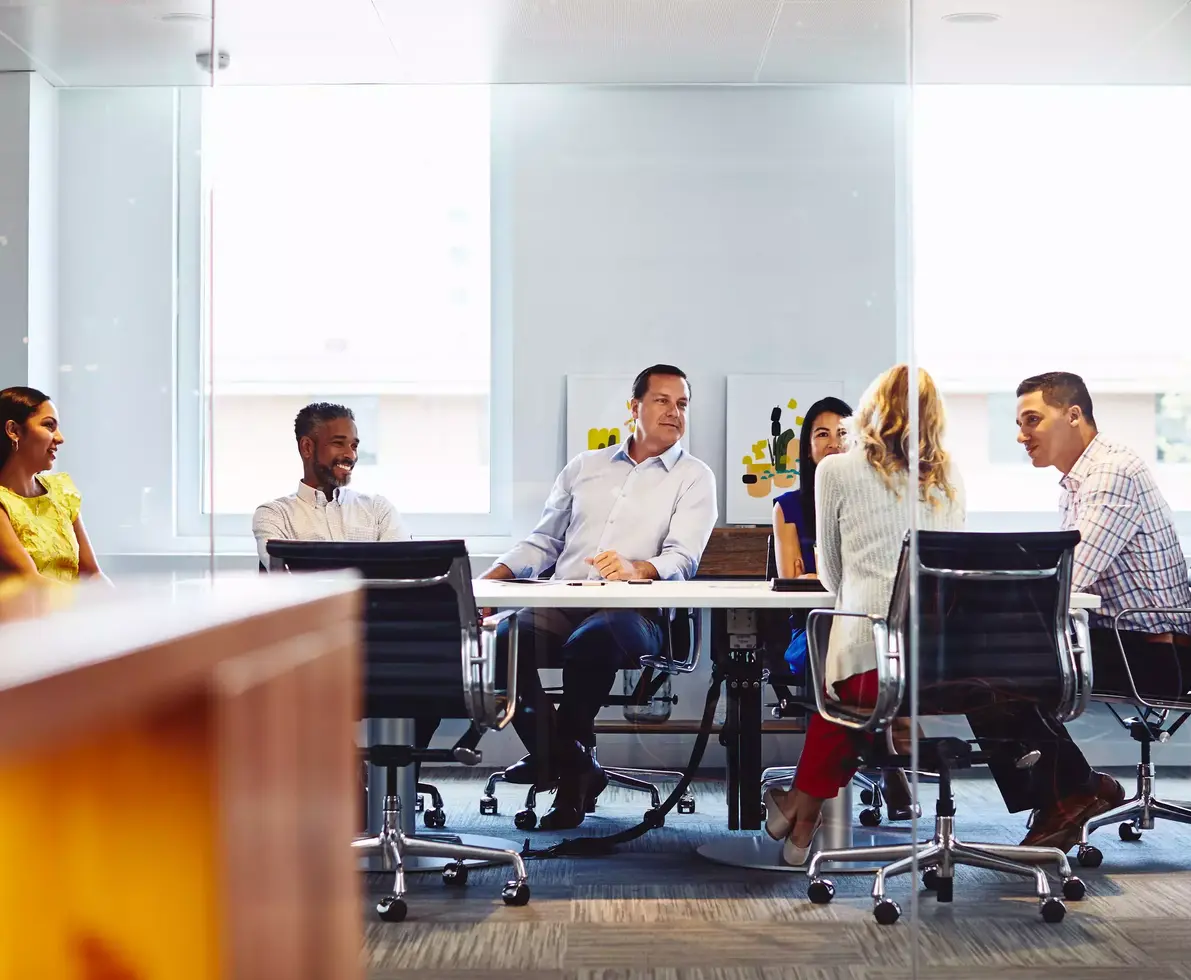 Group of colleagues sitting down in a meeting room at the office, smiling.
