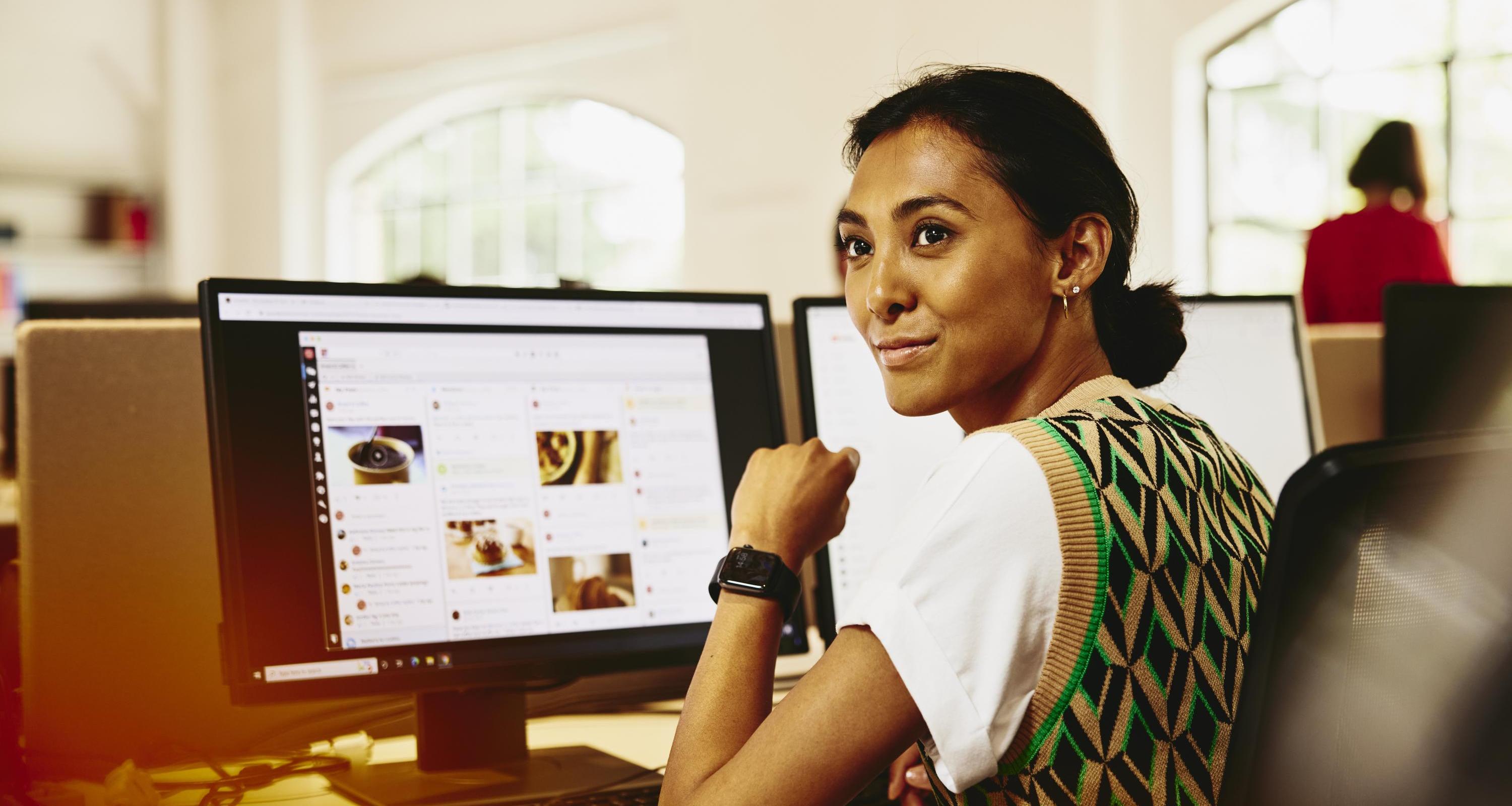 Woman sitting at her desk, looking away from computer screens displaying marketing content.