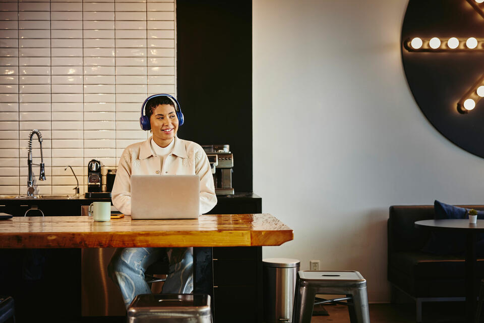 Woman with headphones working on a laptop at a table in a cafe