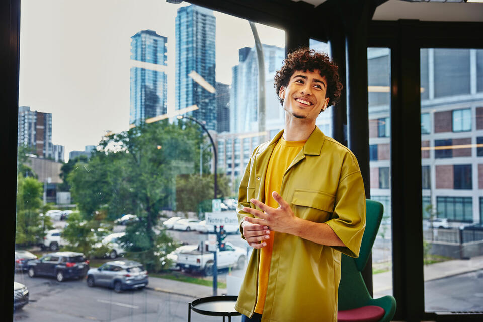 Male in yellow shirt standing at a window, smiling