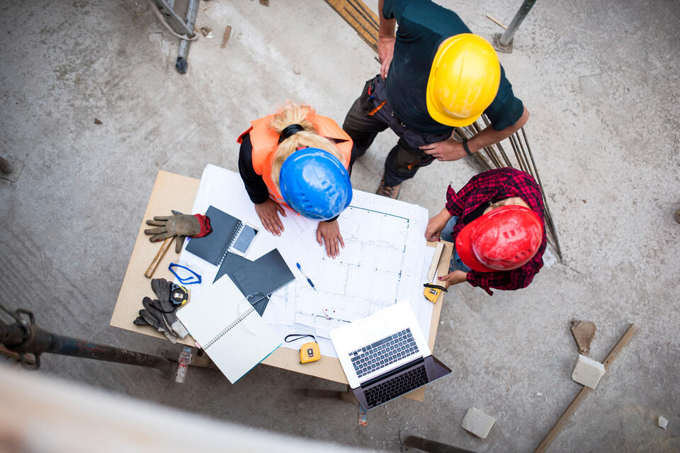 Three workers examining blueprints on a construction site