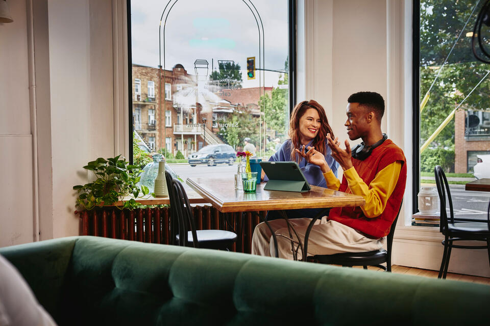 Man and woman sitting next to each other at a table in a cafe with a standing tablet.